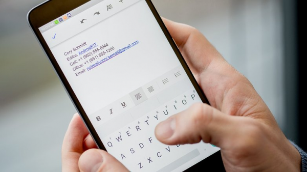 Hands typing a text email signature with name, title, phone numbers and email on an Android phone