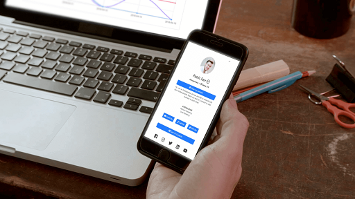 Digital business card open on a smartphone, held in front of a laptop